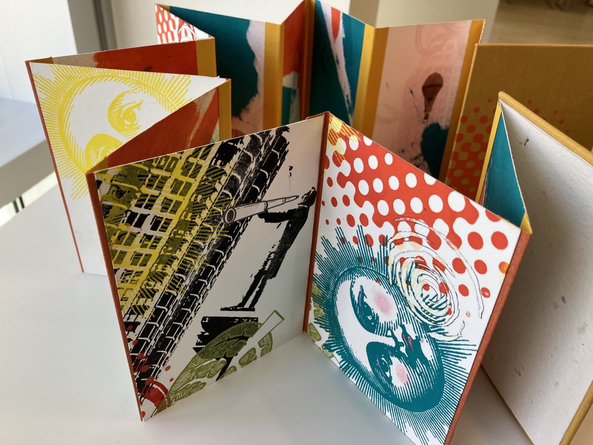 A colorful, accordion-style artist book featuring vibrant illustrations and designs, including suns, faces, and architectural elements. The book is open, revealing dynamic and layered graphics.