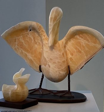 A pair of alabaster sculptures featuring a pelican with outstretched wings and a smaller baby bird, both on separate black bases, capturing a sense of nurturing and protection.