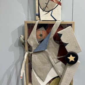 A mixed-media assemblage by Jann Haworth titled "Mannequin Defector," featuring a fragmented figure constructed from canvas, fabric, and wood, with geometric and abstract elements.