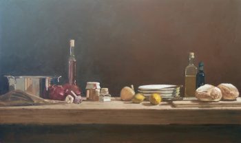 A still-life painting of a rustic kitchen scene with a wooden table set against a dark background. The table holds ingredients such as onions, garlic, lemons, bread, bottles of oil and vinegar, and a stainless steel pot, along with stacked plates and a cookbook.