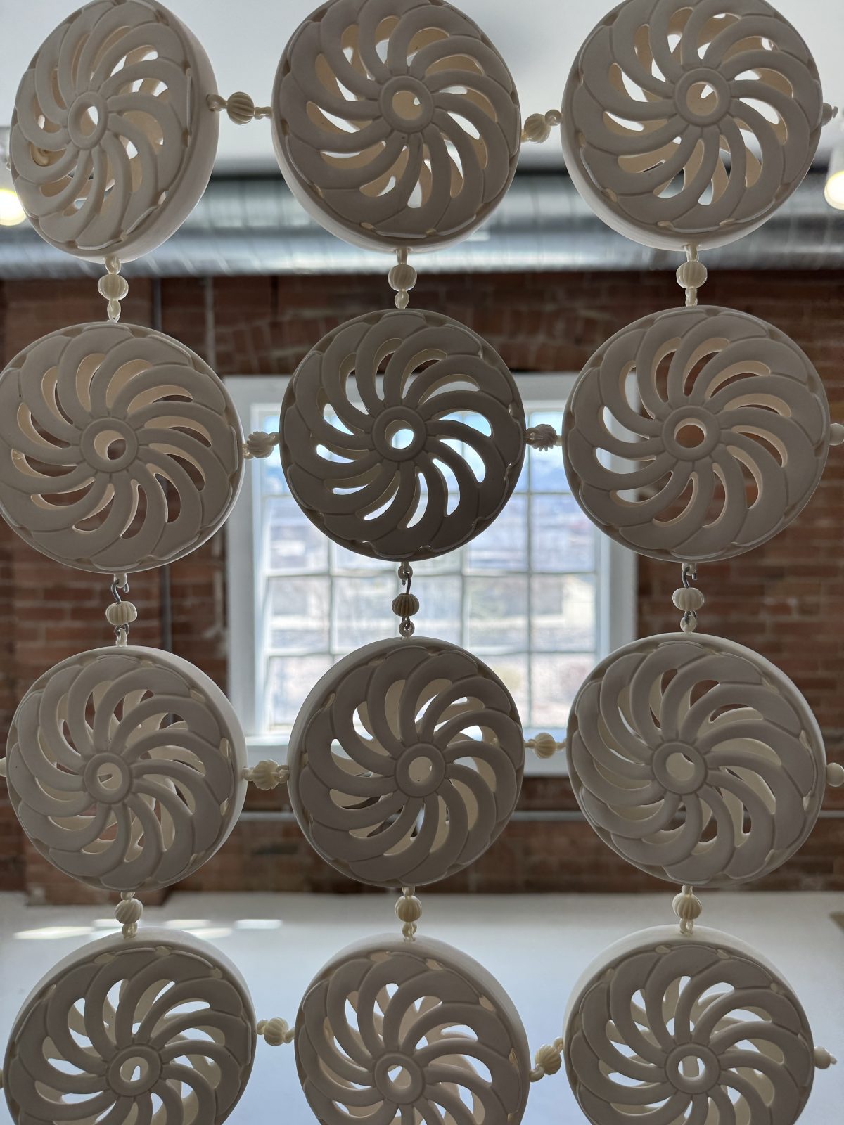 Hanging ceramic installation composed of round white frames enclosing triangular sections of brightly colored fabric or glaze, arranged in a geometric grid.