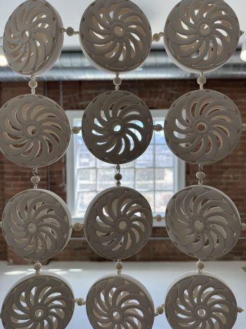 Hanging ceramic installation composed of round white frames enclosing triangular sections of brightly colored fabric or glaze, arranged in a geometric grid.