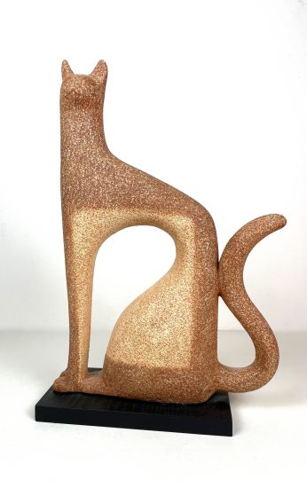 A stylized cat sculpture with a textured bronze-like surface, featuring an elongated body, curved tail, and triangular ears, displayed on a black platform.