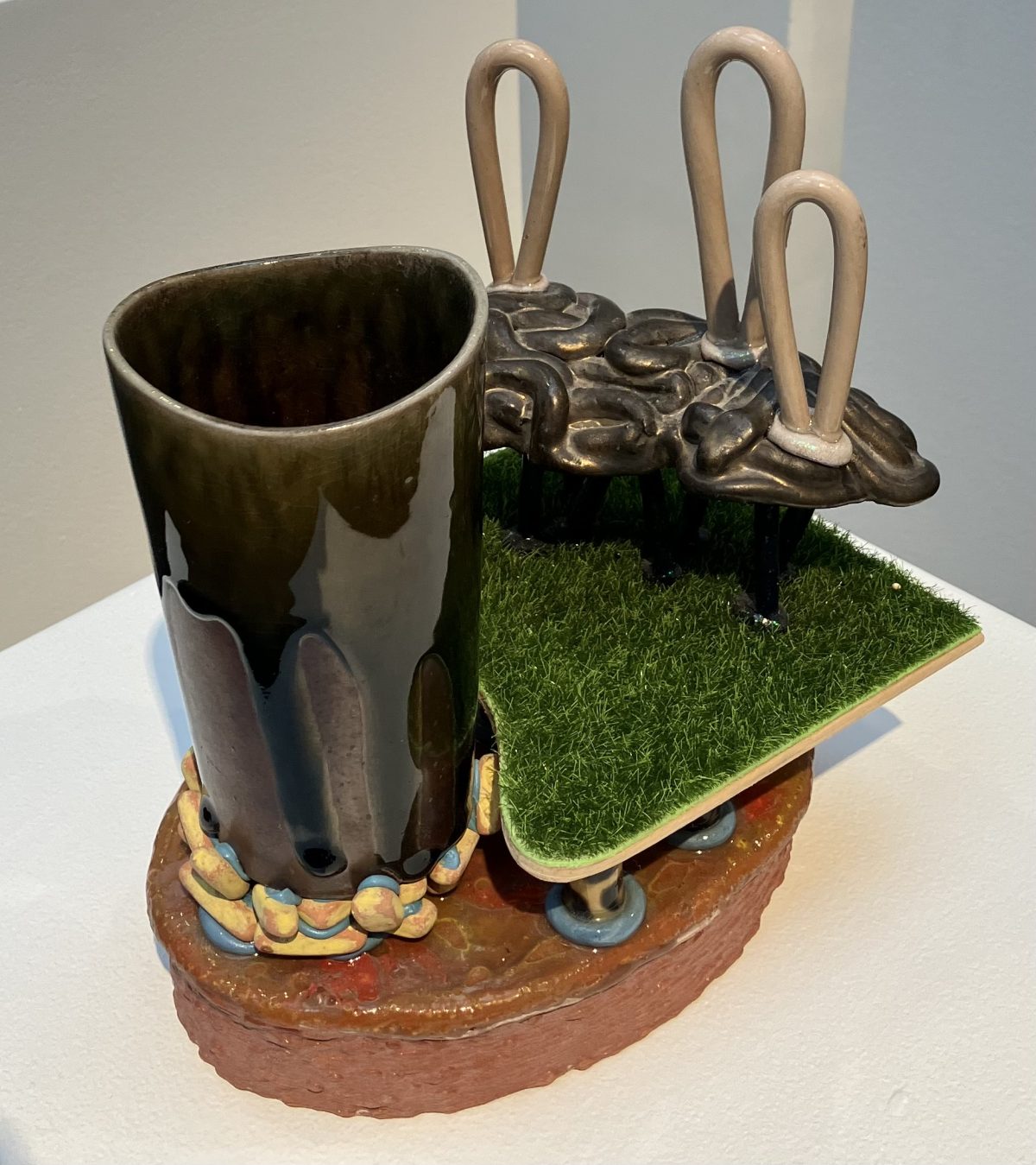 A contemporary ceramic composition featuring a mug-like structure with an attached, organic sculptural element and a smooth black-glazed finish.