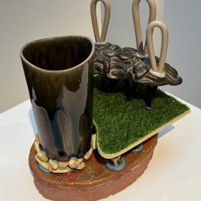 A contemporary ceramic composition featuring a mug-like structure with an attached, organic sculptural element and a smooth black-glazed finish.