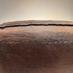 A close-up view of a textured ceramic vessel’s rim, showcasing hand-carved patterns and earthy surface tones.