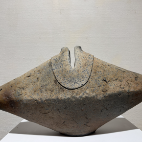 A ceramic sculpture with an angular, geometric form and a textured, speckled surface.