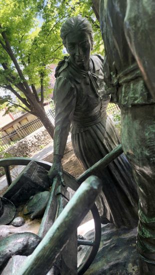 Close-up of a bronze statue of a pioneer woman grasping a handcart, part of a sculpture in Brigham Young Historic Park.