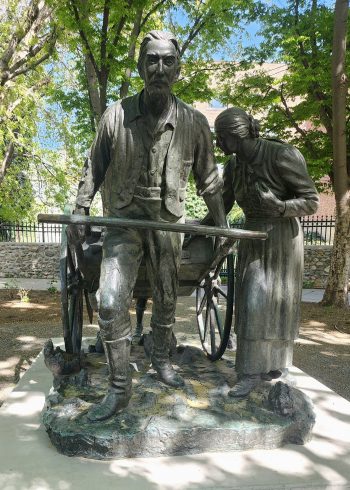 Full view of a bronze sculpture depicting a pioneer man pulling a handcart with a woman at his side, symbolizing Mormon pioneers’ westward journey.