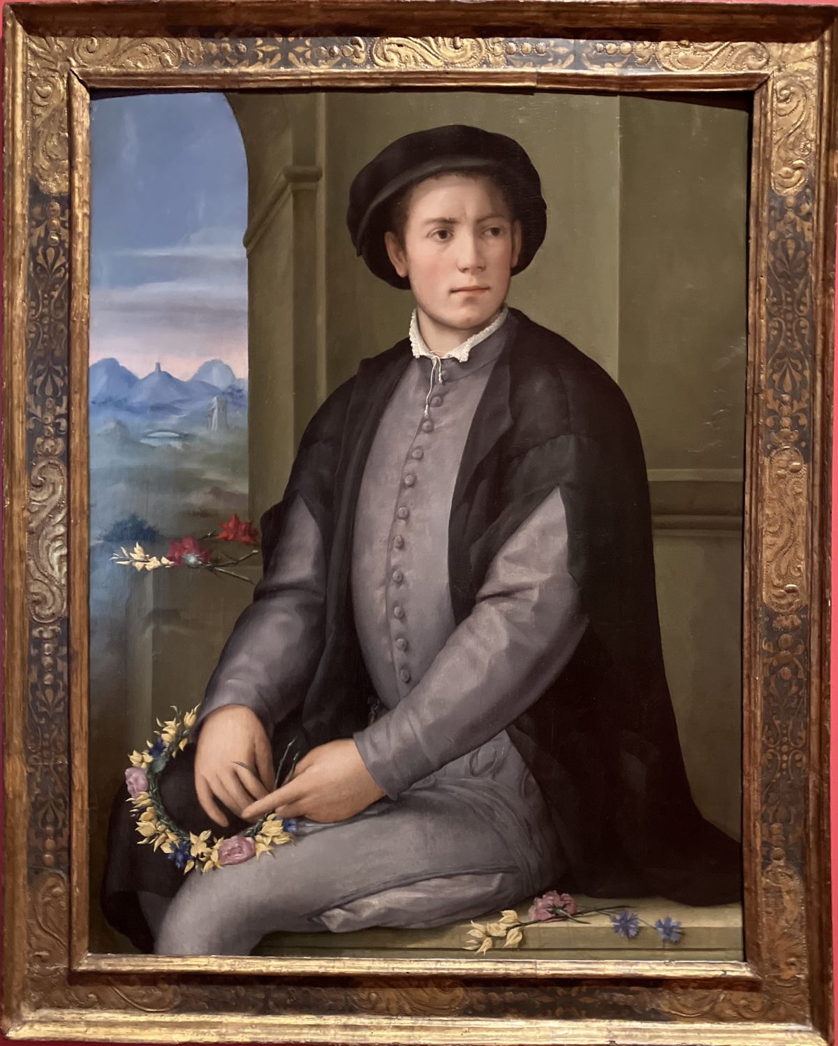 A Renaissance-style portrait of a young man seated, weaving a garland of flowers in his lap.