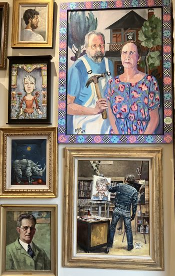 A salon-style installation featuring portraits in a variety of formats, including a man painting a caricatured image of himself.