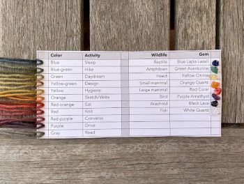 A printed chart showing yarn colors, associated activities, wildlife, and corresponding gemstones, each color represented by a strand of yarn on the left side.