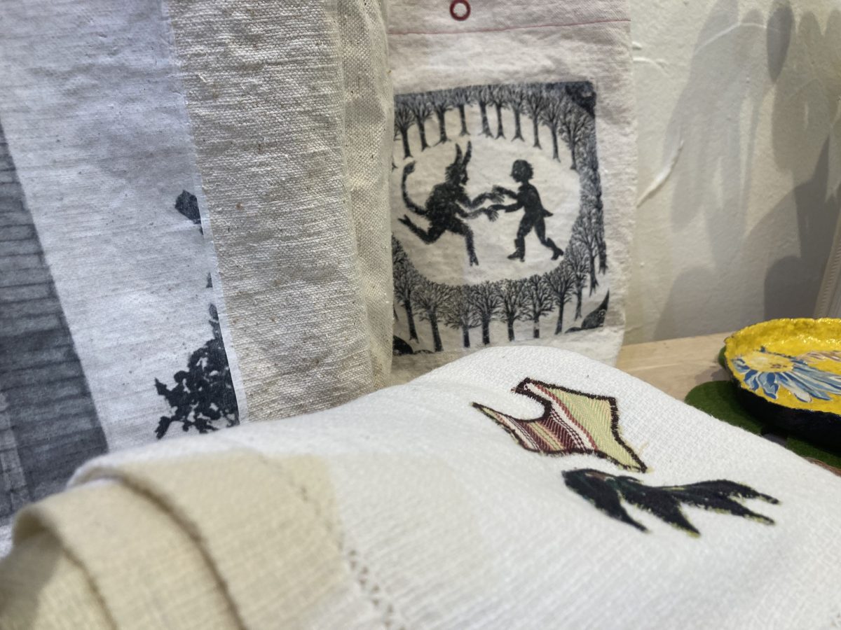Detail of Fern & Reed’s fabric works showing a printed tote with a lighthouse, a pouch with a silhouette print of children, and a towel with appliquéd shapes.