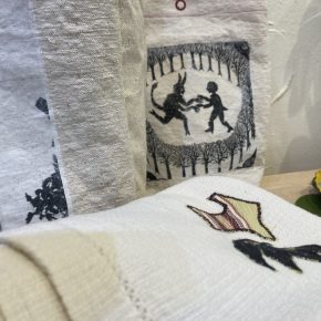 Detail of Fern & Reed’s fabric works showing a printed tote with a lighthouse, a pouch with a silhouette print of children, and a towel with appliquéd shapes.