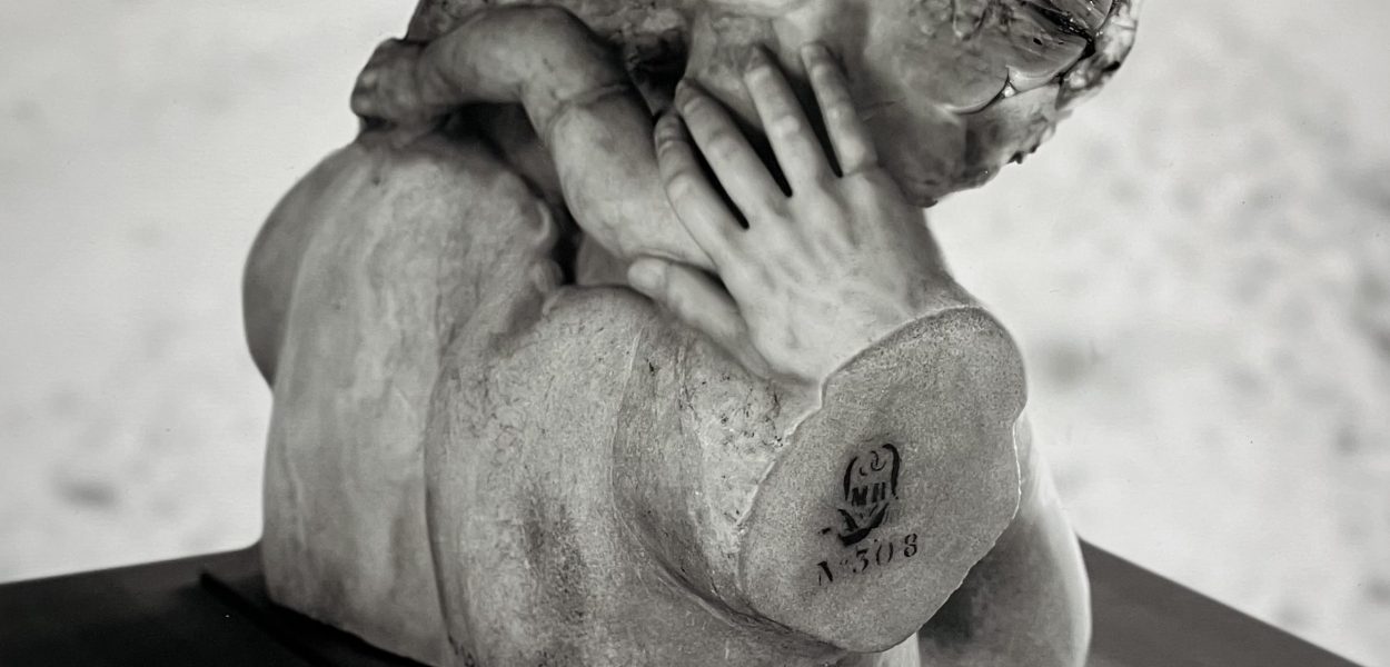 Photograph of a distorted sculpture with overlapping human limbs and facial features, mounted on a pedestal, with printed inventory markings visible.