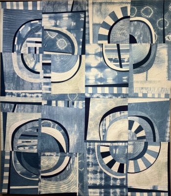 Abstract quilt in shades of indigo and white featuring circular, striped, and tie-dye-inspired patterns arranged in a patchwork grid.