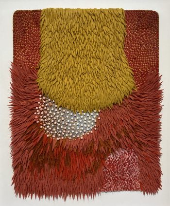 A richly textured mixed-media wall piece of layered felt in deep red, mustard yellow, and gray, with dense tufting and small bead-like forms, creating a tactile, organic surface that feels simultaneously alive and abstract.