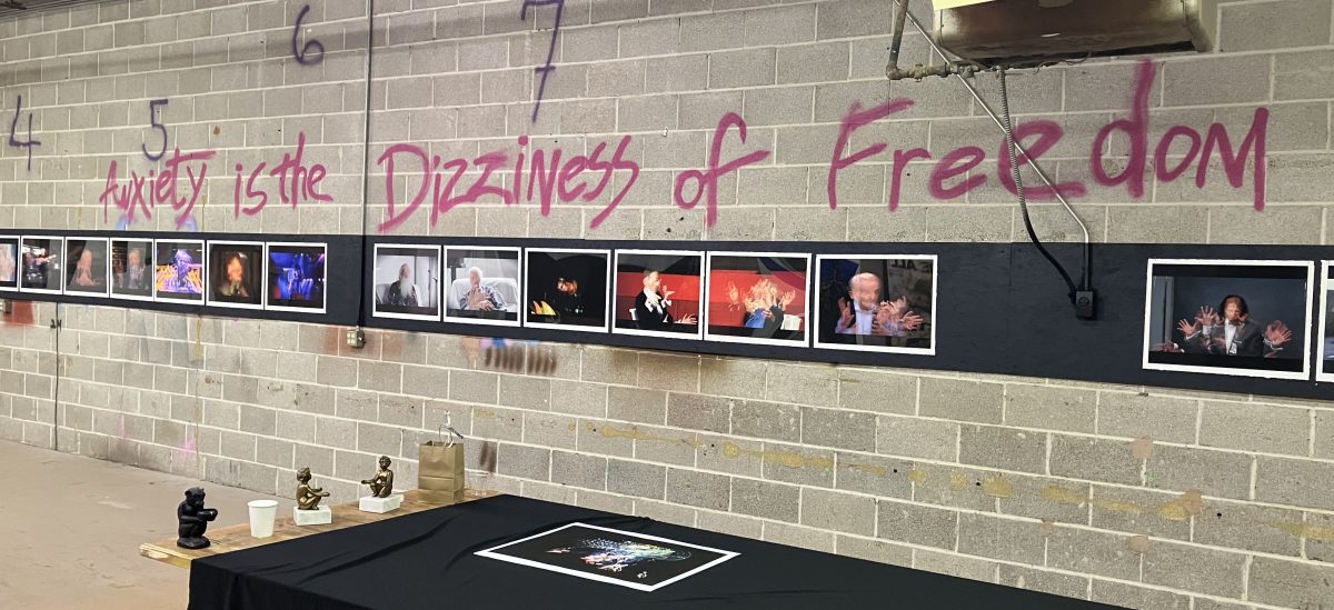 Installation view of John Bell’s Anxiety is the Dizziness of Freedom with 24 photographs mounted in sequence on a cinderblock wall beneath pink spray-painted title text.