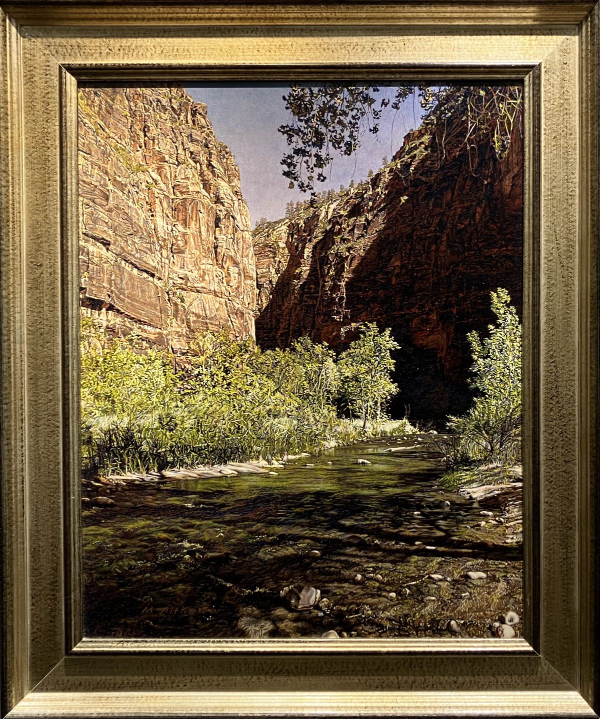 Oil painting of a narrow Zion canyon by Michael Aitken with green shrubs along a shallow stream and towering rust-colored cliffs descending into shadow.
