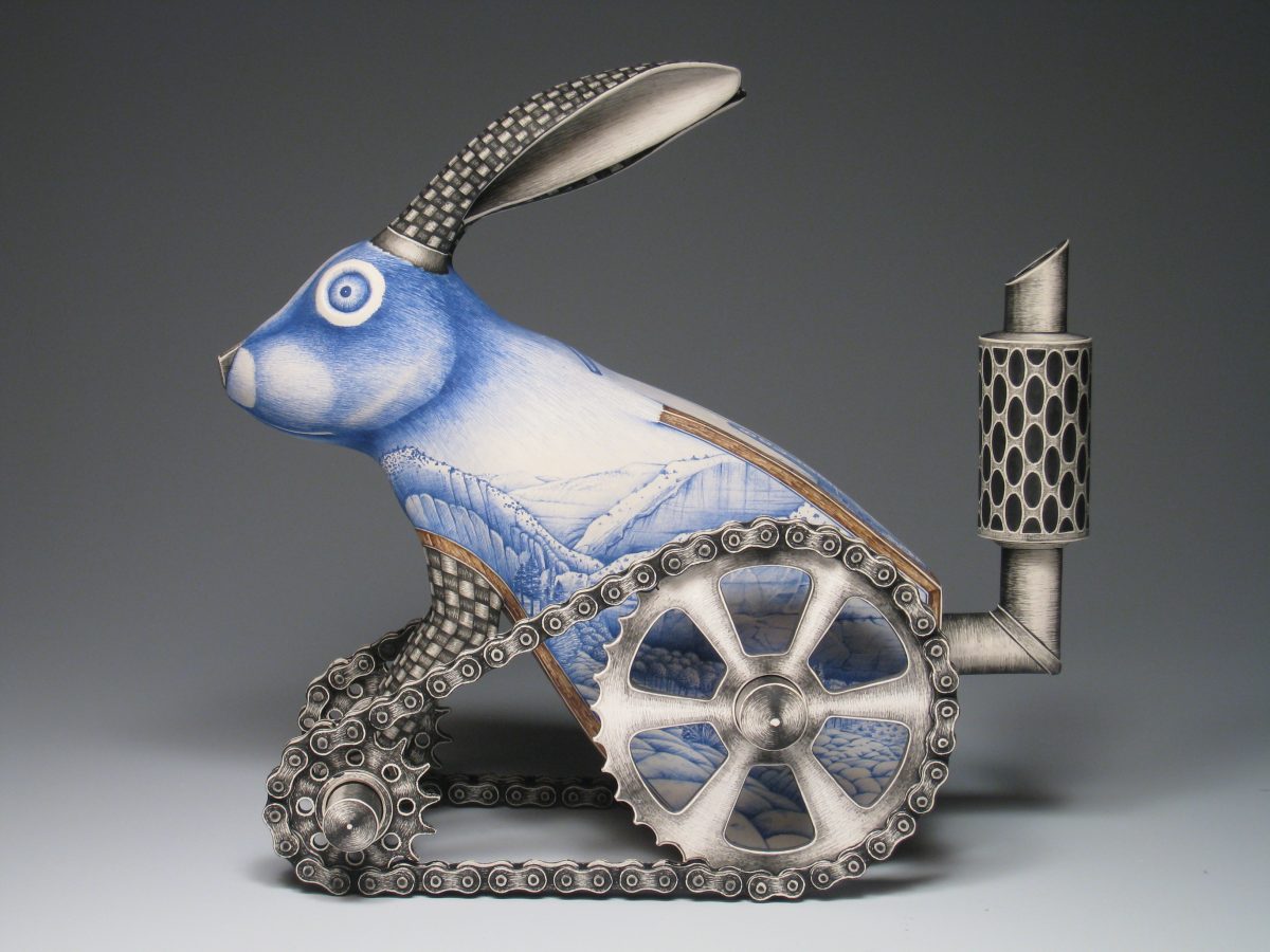 A ceramic sculpture of a blue rabbit fused with metallic tank-like wheels and pipes, its body decorated with delicate landscape drawings.
