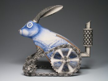 A ceramic sculpture of a blue rabbit fused with metallic tank-like wheels and pipes, its body decorated with delicate landscape drawings.