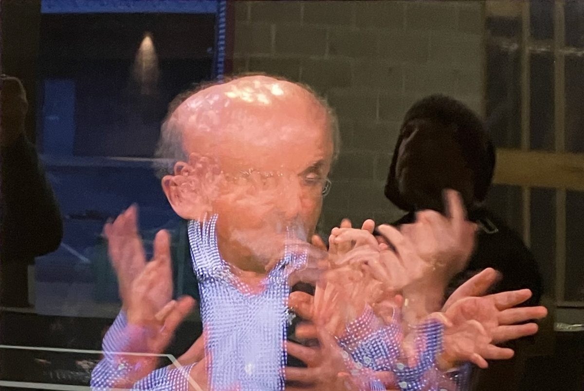 Photographic portrait of Salman Rushdie composed of repeated, overlapping frames of his face and hands in motion.